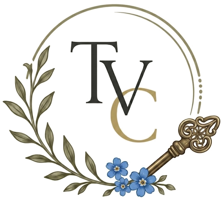 The Village Collective logo: an open olive wreath around the letters T V C, with a brass key and forget-me-nots